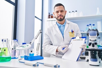 Sticker - Hispanic man working at scientist laboratory holding blank clipboard skeptic and nervous, frowning upset because of problem. negative person.