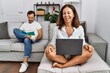 © Krakenimages.com - Hispanic middle age couple at home, woman using laptop winking looking at the camera with sexy expression, cheerful and happy face.