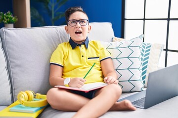 Poster - Young hispanic kid doing homework sitting on the sofa angry and mad screaming frustrated and furious, shouting with anger. rage and aggressive concept.