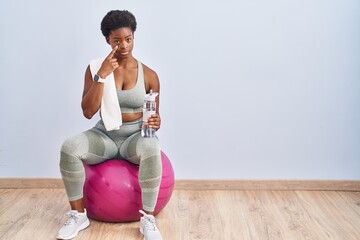 Poster - African american woman wearing sportswear sitting on pilates ball pointing to the eye watching you gesture, suspicious expression