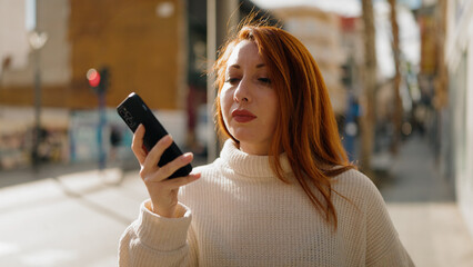 Wall Mural - Young redhead woman using smartphone at street