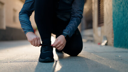 Wall Mural - Young redhead woman wearing sportswear tying shoes at street