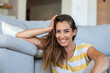 © Graphicroyalty - Happy young woman sitting on sofa at home and looking at camera. Portrait of beautiful woman smiling and relaxing during summer.