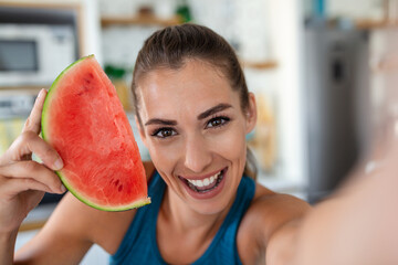 Wall Mural - Young woman eats a slice of watermelon in the kitchen. Portrait of young woman enjoying a watermelon.