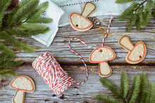 Overhead View Of Gingerbread Mushroom Cookie Decorations In A Glass Dish With Fir Branches, String, Scissors And A Lace Tablecloth