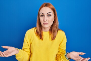 Sticker - Young woman standing over blue background clueless and confused with open arms, no idea concept.