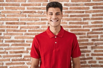 Wall Mural - Young hispanic man standing over bricks wall with a happy and cool smile on face. lucky person.