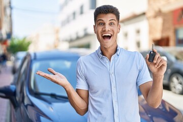 Young hispanic man holding car key celebrating achievement with happy smile and winner expression with raised hand