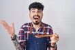 © Krakenimages.com - Young hispanic man with beard wearing apron tasting food holding wooden spoon celebrating victory with happy smile and winner expression with raised hands
