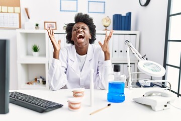 Sticker - African dentist woman working at medical clinic celebrating mad and crazy for success with arms raised and closed eyes screaming excited. winner concept