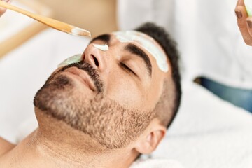 Canvas Print - Young hispanic man having facial mask treatment at beauty center