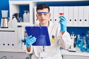 Poster - Young non binary man scientist reading report holding urine test tube at laboratory