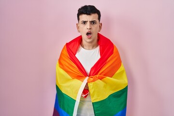 Sticker - Non binary person holding rainbow lgbtq flag scared and amazed with open mouth for surprise, disbelief face