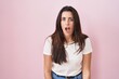 Young brunette woman standing over pink background afraid and shocked with surprise and amazed expression, fear and excited face.