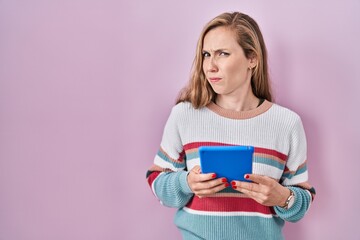 Poster - Young blonde woman holding touchpad clueless and confused expression. doubt concept.