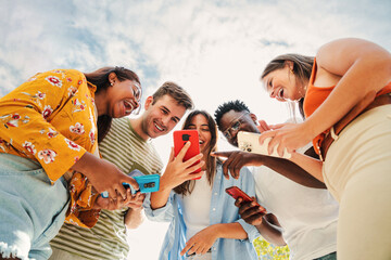 low angle view of a group of smiling multiracial teenagers addicted to smartphones, watching funny v