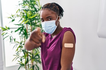 Canvas Print - Beautiful black woman getting vaccine showing arm with band aid pointing with finger to the camera and to you, confident gesture looking serious