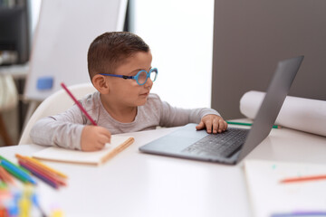 Poster - Adorable hispanic toddler student using laptop drawing on notebook at classroom