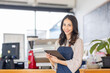 © David - Portrait young Asian woman barista feeling happy smiling at urban cafe. Small business owner Asian girl in apron at small business entrance.