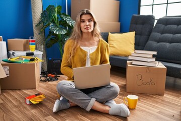 Sticker - Young woman sitting on the floor at new home using laptop relaxed with serious expression on face. simple and natural looking at the camera.