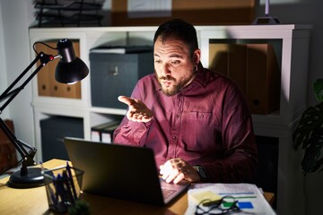 Wall Mural - Plus size hispanic man with beard working at the office at night looking at the camera blowing a kiss with hand on air being lovely and sexy. love expression.