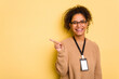 © Asier - Young brazilian woman with a badge isolated on yellow background smiling and pointing aside, showing something at blank space.