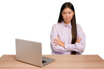 Young student asian woman in a workplace with a laptop isolated frowning face in displeasure, keeps arms folded.