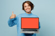 © ViDi Studio - Young smiling happy smart IT woman wear knitted sweater hold use work on laptop pc computer with blank screen workspace area show thumb up isolated on plain pastel light blue cyan background studio.