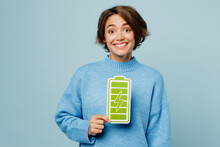 Young Positive Happy Fun Caucasian Woman Wear Knitted Sweater Look Camera Hold In Hand Full Battery Charge Green Card Sign Isolated On Plain Pastel Light Blue Cyan Background People Lifestyle Concept.