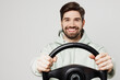 © ViDi Studio - Young smiling happy fun satisfied cheerful caucasian man wear mint hoody look camera hold steering wheel driving car isolated on plain solid white background studio portrait. People lifestyle concept.