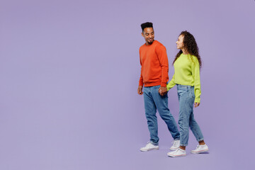 Wall Mural - Full body side view young couple two friends family man woman of African American ethnicity wear casual clothes hold hands walk go strolling together isolated on pastel plain light purple background.