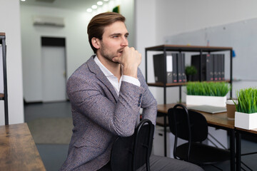 a business man in a jacket sits on a chair in the office, thinking, looks ahead