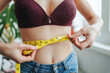 Unrecognizable young girl woman on diet measures her waist with centimeter tape. Woman hands hold centimeter tape. Result is unknown. Close up. Beauty and weight loss concept