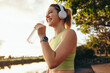 © Jacob Lund - Female athlete taking a break outdoors, drinking water and listening to music with headphones