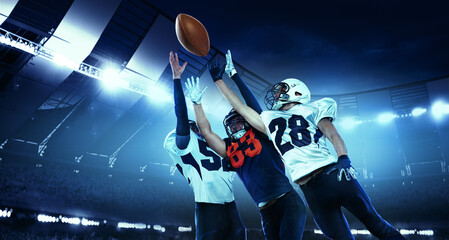 In a jump. Three active american football players in motions, playing, catching ball isolated at the stadium with flashlights