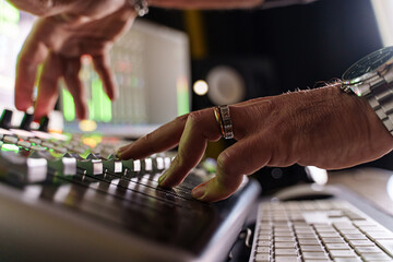 Wall Mural - Close-up of caucasian music producer fading volume on sound mixer control panel in small music production studio - audio engineer at work -