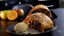 Delicious fresh strudel stuffed with apples and raisins, served with a ball of ice cream, beautiful dessert, black background