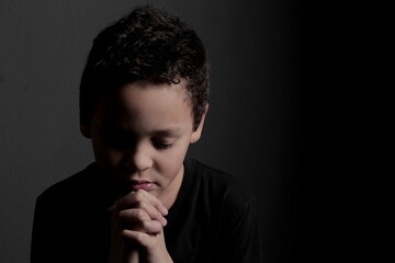 Wall Mural - little boy praying to God with hands together with black background stock photo