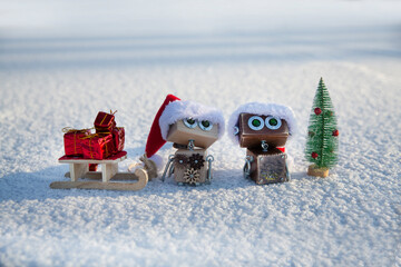 two wooden robots in Santa red hat with gifts and Christmas tree in the snow. santa assistants. copy space