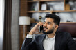 © sofiko14 - Close up portrait of cheerful bearded male boss in business suit talking using smartphone during break and smiling. Confident man team leader giving consultations with phone in modern company office.
