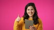 © Robert Peak - Portrait of happy smiling young woman 20s in sweater shopping on tablet computer give thumbs up gesture isolated on pink background studio.