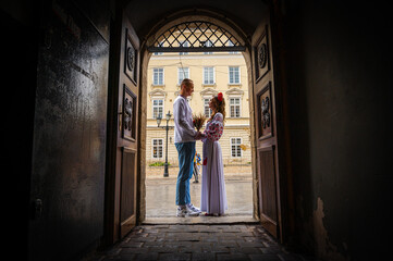 Wall Mural - Profile view of a young couple in love in Ukrainian national dress in an embroidered shirt embracing while standing in a doorway. View from the corridor through the doorway. Creating a family