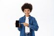 Online shopping. Smiling african american girl pointing at her mobile phone screen, showing smartphone app interface, white background