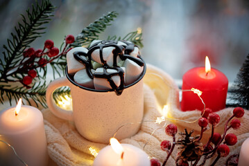 Wall Mural - Winter Christmas holidays background with candles; christmas light; Cup of cocoa with marshmallow or hot chocolate near a window