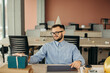 © dsheremeta - Happy positive bearded office worker in cone hat sitting at workplace with laptop and gift with festive ribbon.