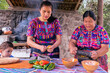 Retrato de madre enseñando a su hija a cocinar con una piedra de moler y una vajilla de arcilla. Mujeres Latinas.