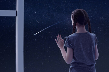 little girl near window looking at shooting star in beautiful night sky