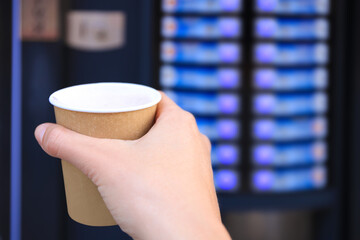 Poster - Man holding paper cup with hot drink near coffee vending machine, closeup. Space for text