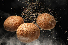Flying burger buns with sesame and smoke on black background