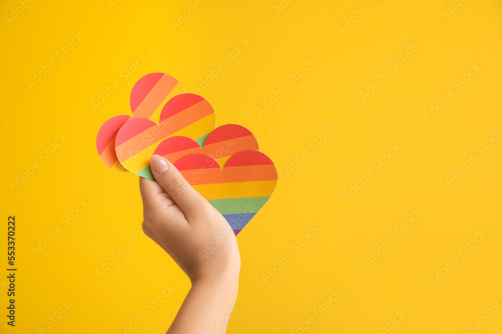 Female hand with rainbow hearts on yellow background. LGBT concept
